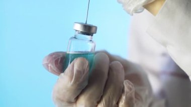 Doktorun elleri mavi arka planda aşı için aşı hazırlıyor.