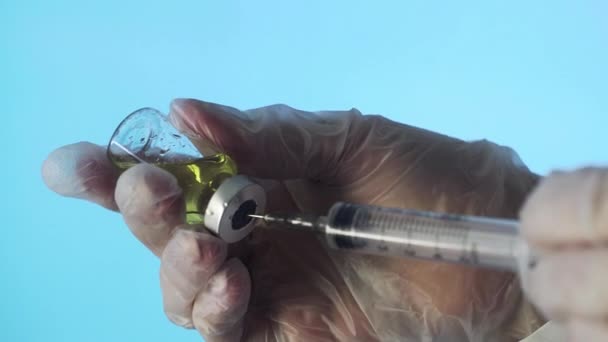 Gros plan des mains d'un médecin préparant un vaccin injectable sur fond bleu — Video