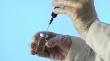Doktorların elleri temiz çözeltili bir şırınga tutarken ve ampulün içine kırmızı bir madde dökerken. Bir tıp laboratuarında aşı geliştirme süreci, deneysel araştırmalar.