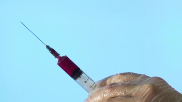 Close-up of a needle from a disposable syringe. A small syringe pushes a red liquid out of the hole on a blue background — Stock Video