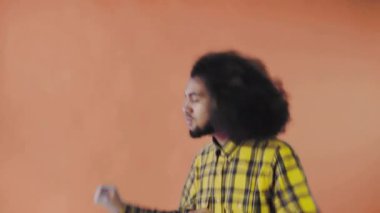 Turuncu arka planda Afrikalı saç stili olan genç bir adam dans ediyor. Renkli bir arkaplanda dans etmek.