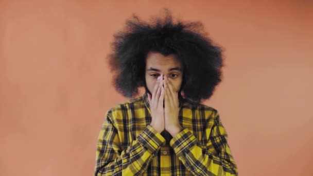 En ung mand med en afrikansk frisure på en orange baggrund er overrasket. Følelser på en farvet baggrund. – Stock-video