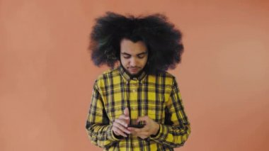 Turuncu arka planda Afrikalı saç stili olan genç bir adam telefonunu çıkardı ama işe yaramadı. Renkli bir arkaplanda duygular