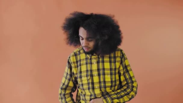 Un giovane con un'acconciatura africana su sfondo arancione tira fuori il telefono, guarda il messaggio e lo rimette in tasca. Emozioni su sfondo colorato — Video Stock
