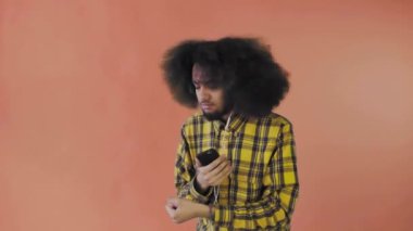 Turuncu arka planda Afrikalı saç stili olan genç bir adam müzik ve kulaklık dinliyor. Renkli bir arkaplanda