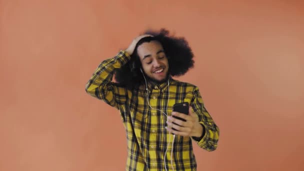 Un giovane con un'acconciatura africana su sfondo arancione in cuffia comunica tramite collegamento video. Su uno sfondo colorato — Video Stock
