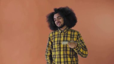 Elinde banknot yelpazesi olan mutlu bir Afro-Amerikalı adam, turuncu bir arka planda izole bir şekilde kameraya bakıyor.