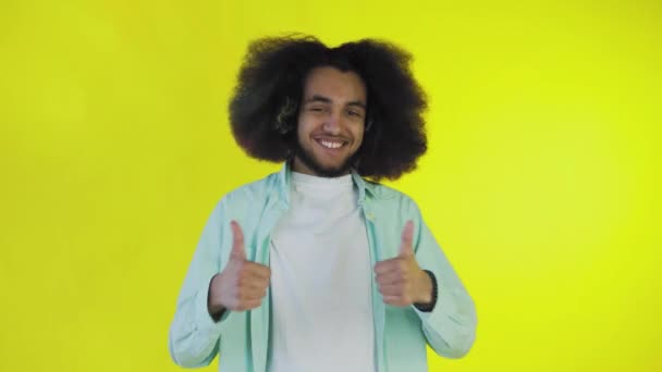 Un hombre afroamericano feliz mirando a la cámara, muestra un parecido con su mano, se encuentra aislado sobre un fondo amarillo — Vídeos de Stock