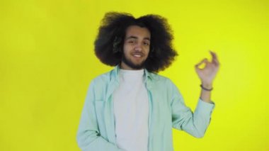 Sarı arka planda Afrikalı saç stili olan genç bir adam iyi bir jest gösteriyor. Renkli bir arkaplanda duygular.