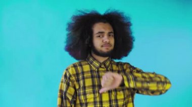 Afro-Amerikalı bir adam kameraya bakar, başparmağını kaldırır, mavi bir arka planda tek başına durur.