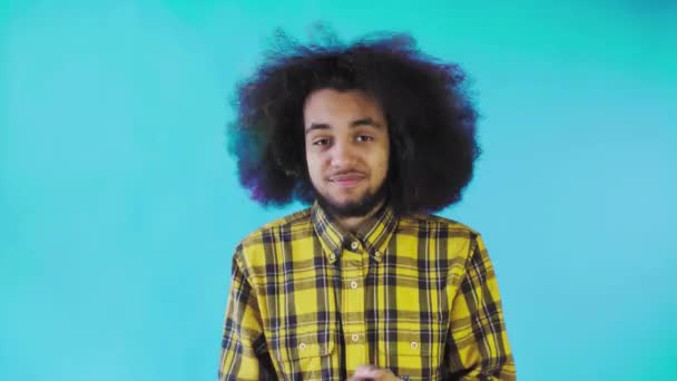 Молодий чоловік з африканською зачіскою на синьому фоні щасливий. Емоції на кольоровому фоні. — стокове відео