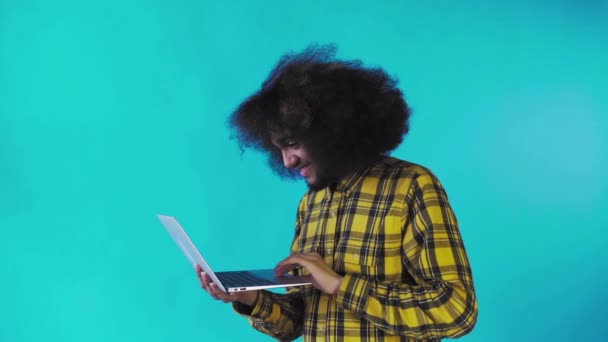 Молодой человек с африканской прической на синем фоне печатает на ноутбуке. На цветном фоне — стоковое видео