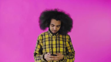 Pembe arka planda Afrikalı saç stili olan genç bir adam telefonuna konuşuyor..
