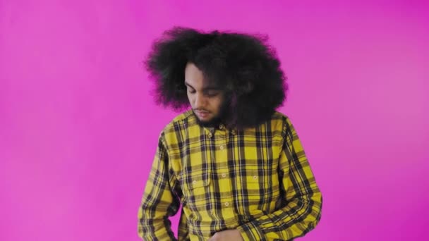 En ung mand med afrikansk frisure på lyserød baggrund tager sin telefon, kigger på beskeden og putter den tilbage i lommen. Følelser på en farvet baggrund – Stock-video