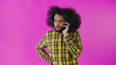 Pembe arka planda Afrikalı saç stili olan genç bir adam telefonda konuşuyor. Renkli bir arkaplanda