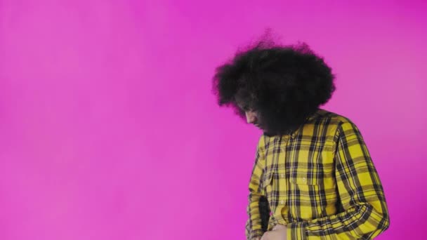 Ein junger Mann mit afrikanischer Frisur auf rosa Hintergrund zückt sein Handy, betrachtet die Nachricht und steckt sie wieder in die Tasche. Emotionen auf farbigem Hintergrund — Stockvideo