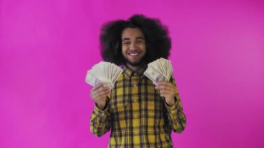 Elinde banknot yelpazesi olan mutlu bir Afro-Amerikalı adam pembe bir arka planda tek başına kameraya bakıyor.