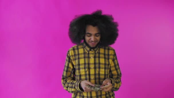 Szczęśliwy Afroamerykanin trzymający banknoty w rękach, liczący je i patrzący w kamerę, stojący samotnie na różowym tle — Wideo stockowe