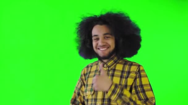 Un hombre afroamericano feliz mirando a la cámara, muestra un parecido con su mano, se encuentra aislado sobre un fondo verde — Vídeos de Stock