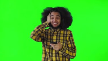 Yeşil arka planda Afrikalı saç stili olan genç bir adam telefona bakar ve mutlu bir şekilde şaşırır. Renkli bir arkaplanda duygular