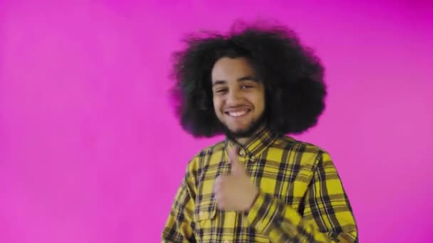 Un uomo afro-americano felice che guarda nella macchina fotografica, mostra un simile con la mano, si trova isolato su uno sfondo rosa — Video Stock