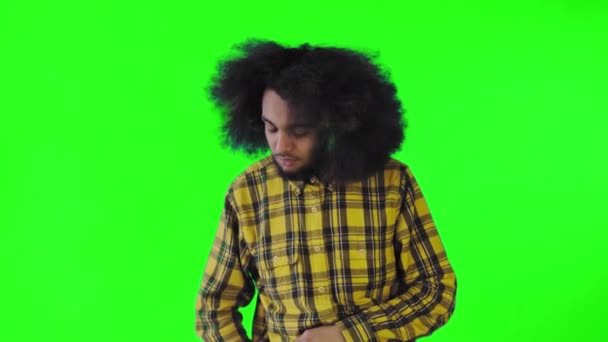 En ung man med en afrikansk frisyr på grön bakgrund tar fram sin telefon, tittar på meddelandet och lägger tillbaka det i fickan. Känslor på en färgad bakgrund — Stockvideo