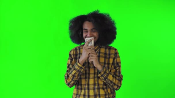 Een gelukkige Afro-Amerikaanse man die bankbiljetten in zijn handen houdt, kust en naar de camera kijkt, staat geïsoleerd op een groene achtergrond — Stockvideo