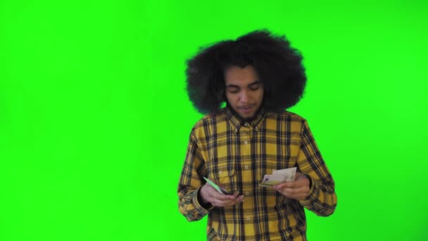 손에 지폐를 들고 숫자를 세고 카메라를 보고 녹색 배경에 고립된 행복 한 흑인 남자 — 비디오
