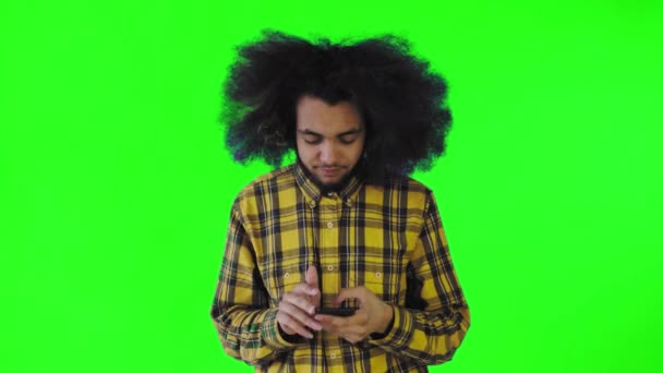 Een jonge man met een Afrikaans kapsel op een groene achtergrond haalt zijn telefoon tevoorschijn, maar het werkt niet. Emoties op een gekleurde achtergrond — Stockvideo
