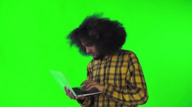 Yeşil arka planda Afrikalı saç stili olan genç bir adam dizüstü bilgisayarda yazıyor. Renkli bir arkaplanda