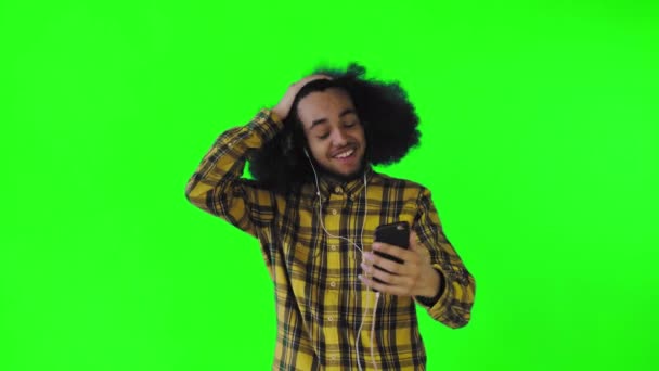 A young man with an African hairstyle on a green background in headphones communicates via video link. On a colored background — Stock Video