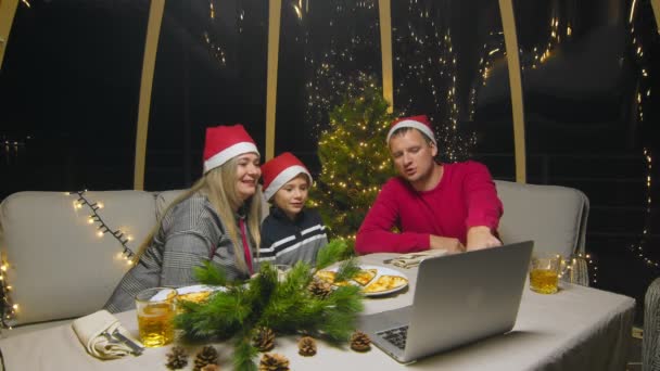 A family with a child, meeting the New Year, sitting at the dinner table. Happy family watching movie on computer during christmas party — Wideo stockowe