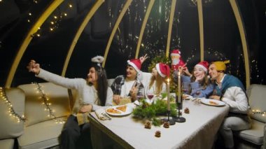 Friends celebrate the New Year at the dinner table. Students taking pictures on the phone during a Christmas party at home