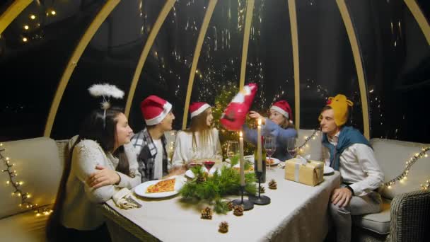 Friends celebrate the New Year at the dinner table. Students during a Christmas party at home. Young people drink wine, eat pizza and give each other gifts — стоковое видео