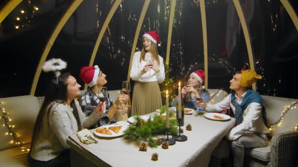 Friends celebrate the New Year at the dinner table. Students during a Christmas party at home. Young people are drinking wine. The girl says a toast — Video Stock