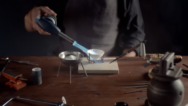 A male jeweler heats metal with a burner. Creating accessories — Vídeos de Stock