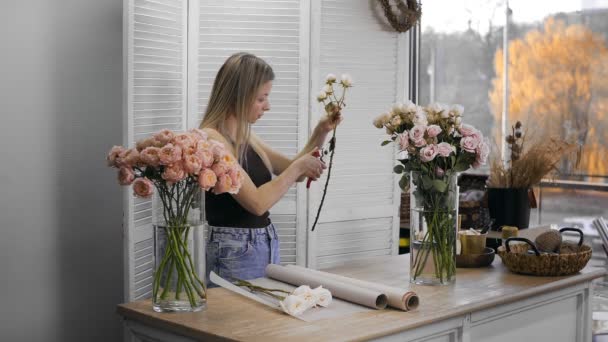 A young beautiful woman engaged in floristry begins to collect the best flowers for her flower arrangement. A girl cuts thorns on roses with a pruner. Floristry — 图库视频影像
