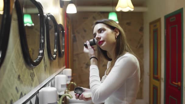 Boční pohled na ženu pomocí pudru s make-up štětcem před zrcadlem, šťastná žena pomocí kosmetiky pro krásu — Stock video