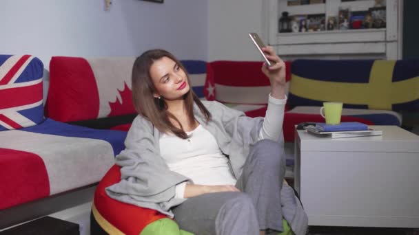 Una joven feliz, sosteniendo un teléfono inteligente moderno y tomando fotos de sí misma. Una chica bonita sonriente mirando un teléfono móvil se toma una selfie — Vídeos de Stock