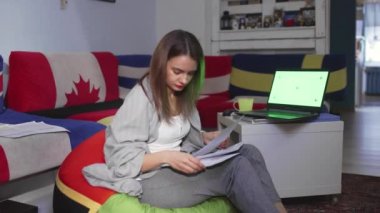 Finansal belgeleri elinde tutan genç bir kadın, internet bankacılığı için dizüstü bilgisayar kullanıyor, faturaları ödüyor dizüstü bilgisayarda çalışıyor, belgeleri işliyor, yeşil ekran üzerinde çalışıyor.