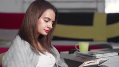Genç bir kadın evinde bir sedirin üzerinde oturuyor ve kitap okuyor. Bir kadın boş zamanlarında rahat bir sedirin üzerinde dinleniyor. Hafta sonları iyi vakit geçir.