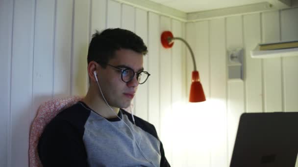 Вид збоку молодий чоловік лежить на ліжку і працює на ноутбуці, друкуючи на клавіатурі, працює вночі, віддалена робота з дому вночі . — стокове відео
