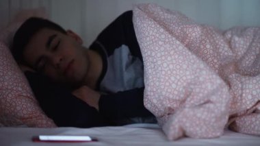 Genç bir adam yatakta uyuyor, gece telefonla bir mesaj alıyor..