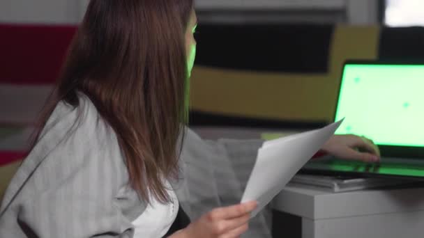 Молодая женщина с финансовыми документами, с помощью ноутбука для интернет-банкинга, оплачивает счета с помощью онлайн-приложения на ноутбуке, работает за компьютером, обрабатывает документы, зеленый экран — стоковое видео
