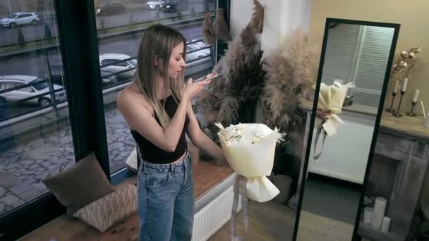 A young beautiful woman engaged in floristry has collected a bouquet of the best flowers and is photographing it on her phone. Floristry — Vídeo de Stock