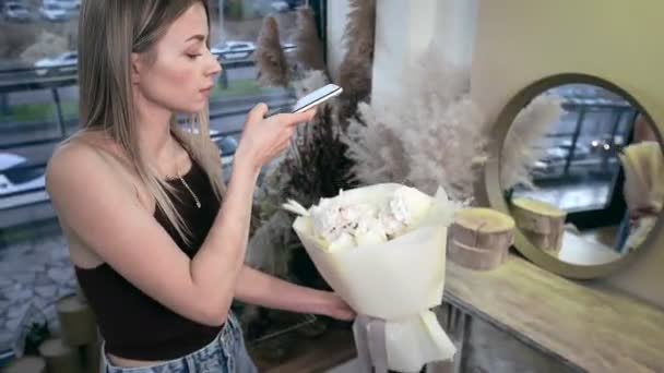 A young beautiful woman engaged in floristry has collected a bouquet of the best flowers and is photographing it on her phone. Floristry — Αρχείο Βίντεο