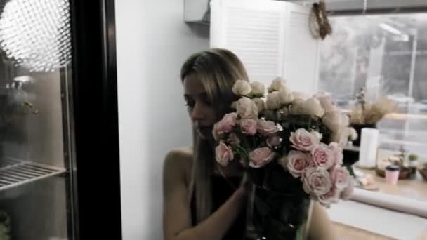 A young beautiful woman is engaged in floristry. The girl takes a bouquet of flowers to the refrigerator. Flower shop. — Video