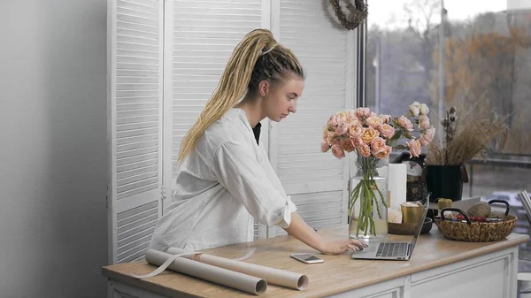 A young beautiful woman engaged in floristry, typing on a computer. Flower shop. — Stock Photo, Image