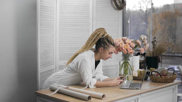Молода, красива жінка займається флористикою, переглядаючи Інтернет на своєму телефоні. Квітковий магазин . — стокове фото