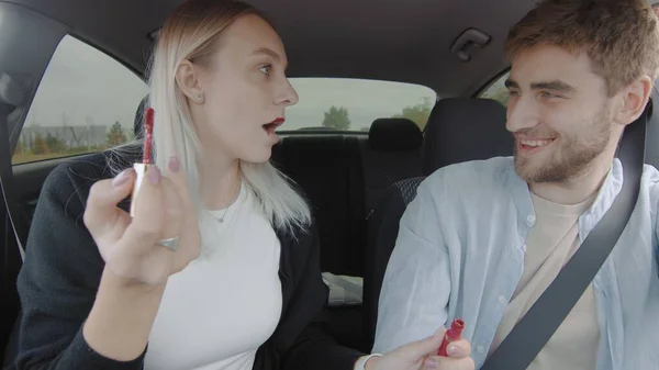 Un tipo y una chica conducen un coche. Una chica se pinta los labios con lápiz labial rojo en el coche. Gente en el coche — Foto de Stock
